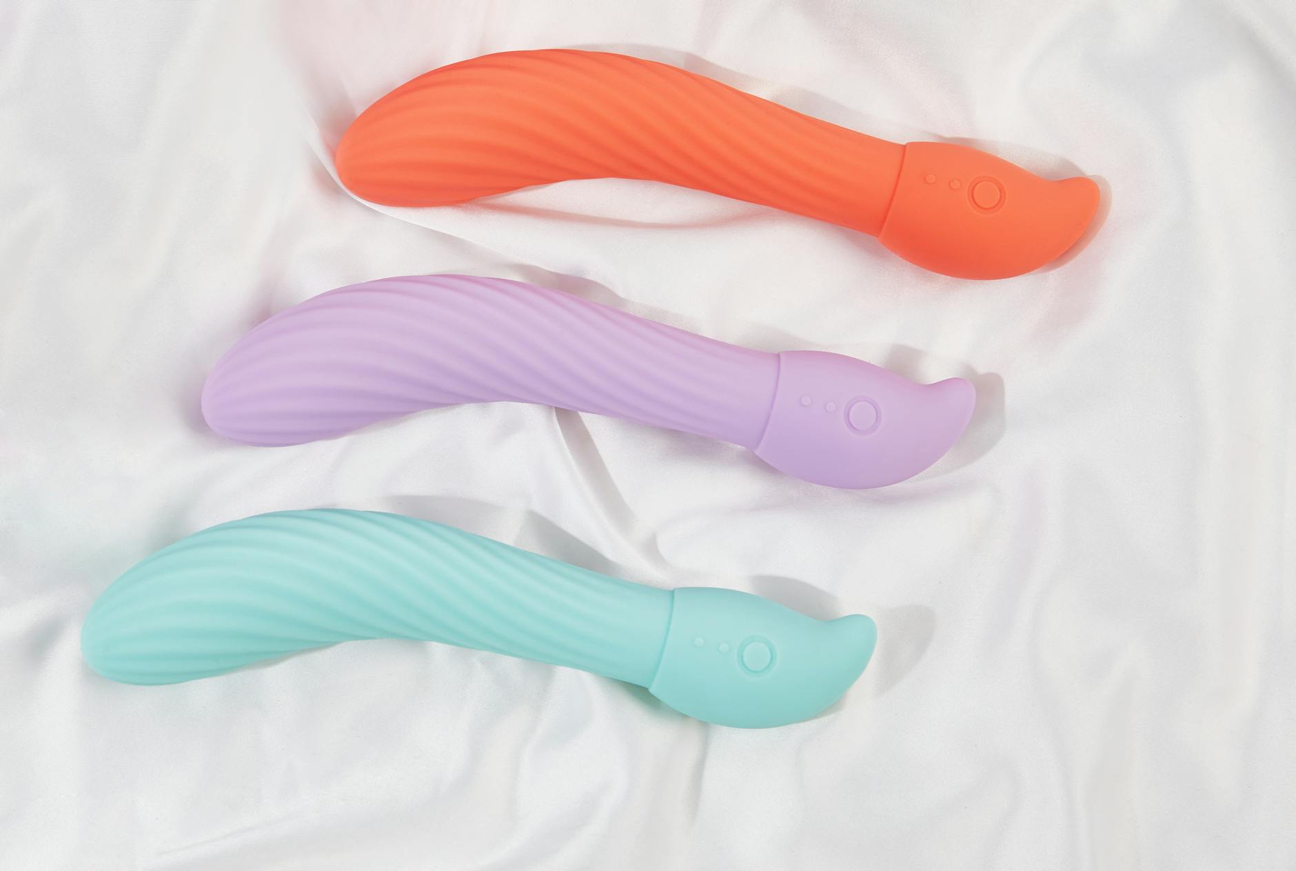 Colorful vibrators arranged on white fabric, highlighting smooth texture.