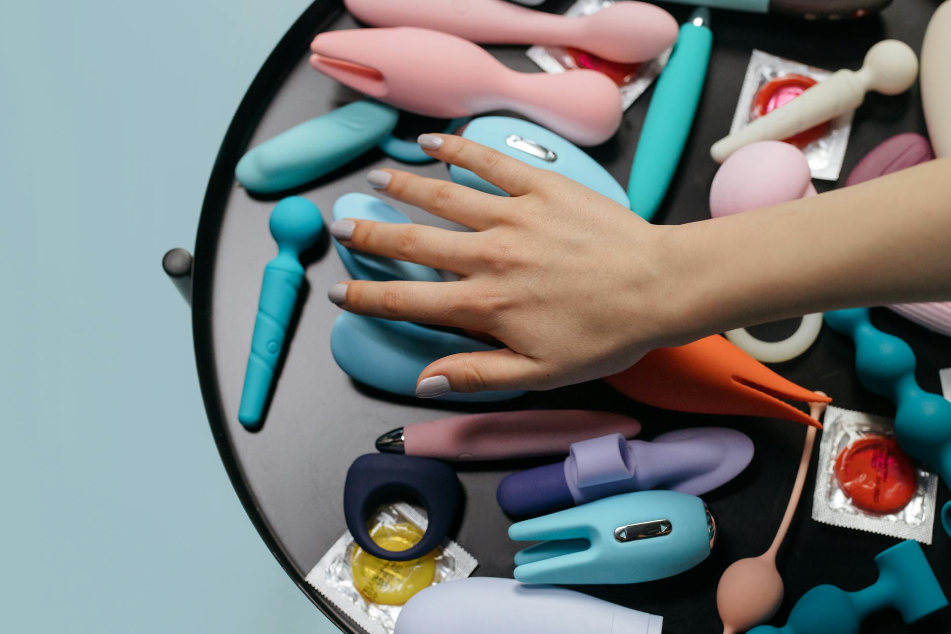 Two hands holding pink and blue silicone vibrators against a pastel background, symbolizing reconnection and pleasure.