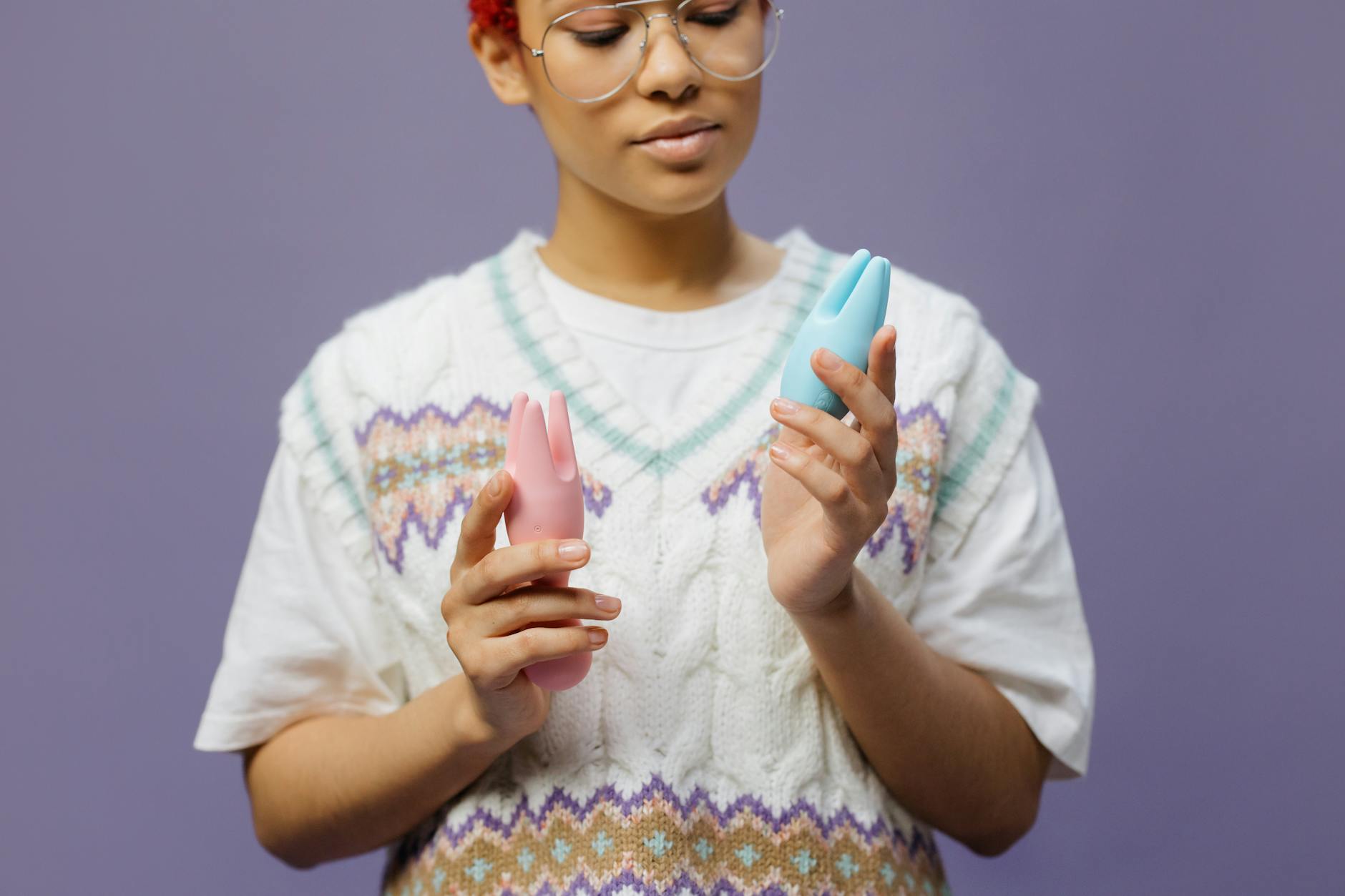 Woman holding blue and pink silicone vibrators in a contemplative moment, representing openness to exploring pleasure together.
