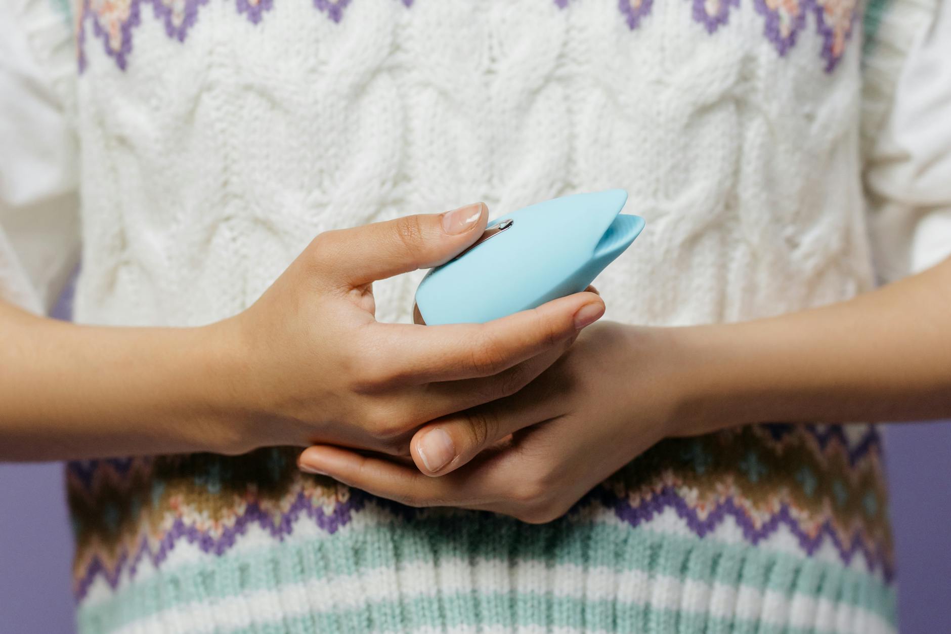 Woman holding a blue personal massager against a knitted sweater, representing intimate exploration with a partner.