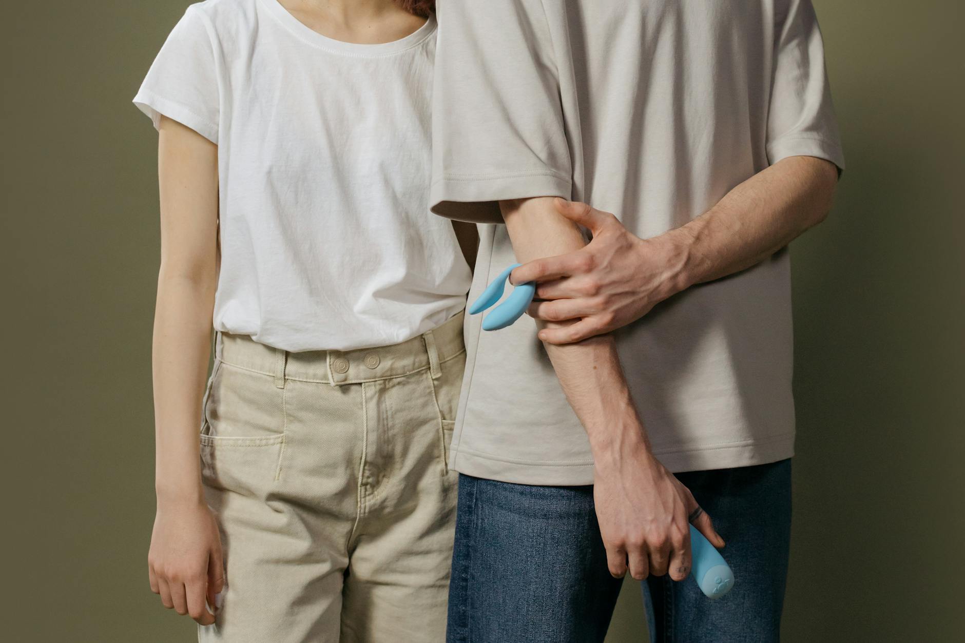 A young couple standing together indoors, holding a blue vibrator, symbolizing modern intimacy